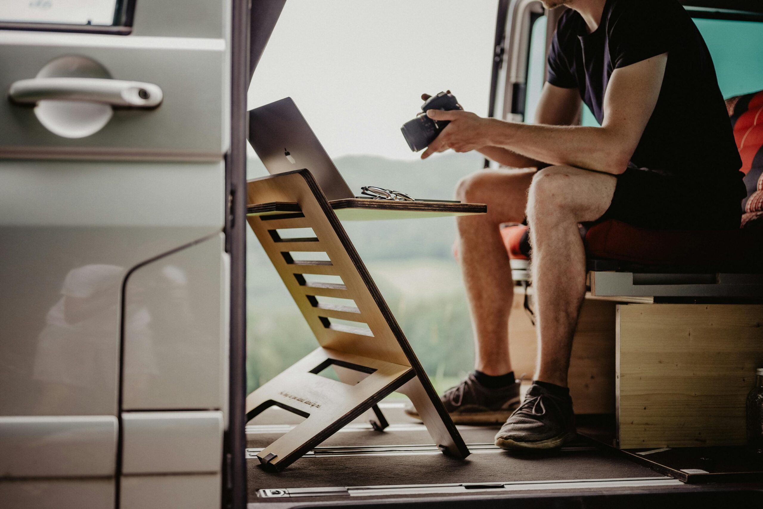 Man working remotely from a van with a portable desk, camera, and laptop setup, emphasizing mobile office lifestyle.