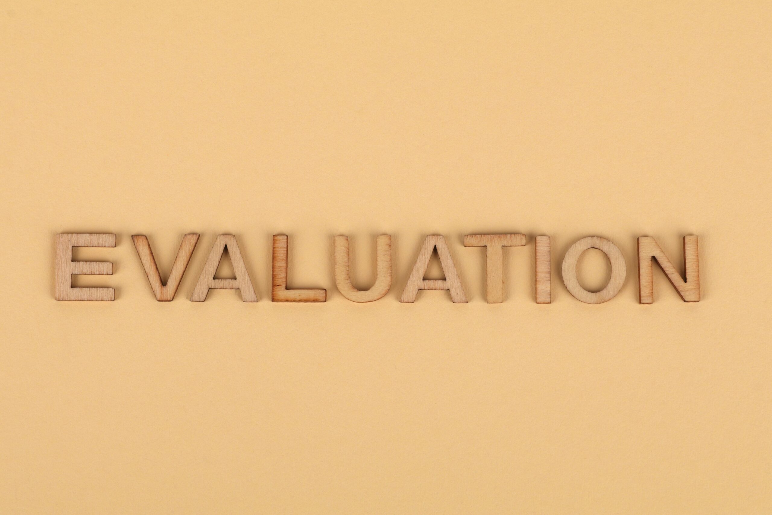 Wooden letter blocks arranged to spell 'evaluation' on a beige background.