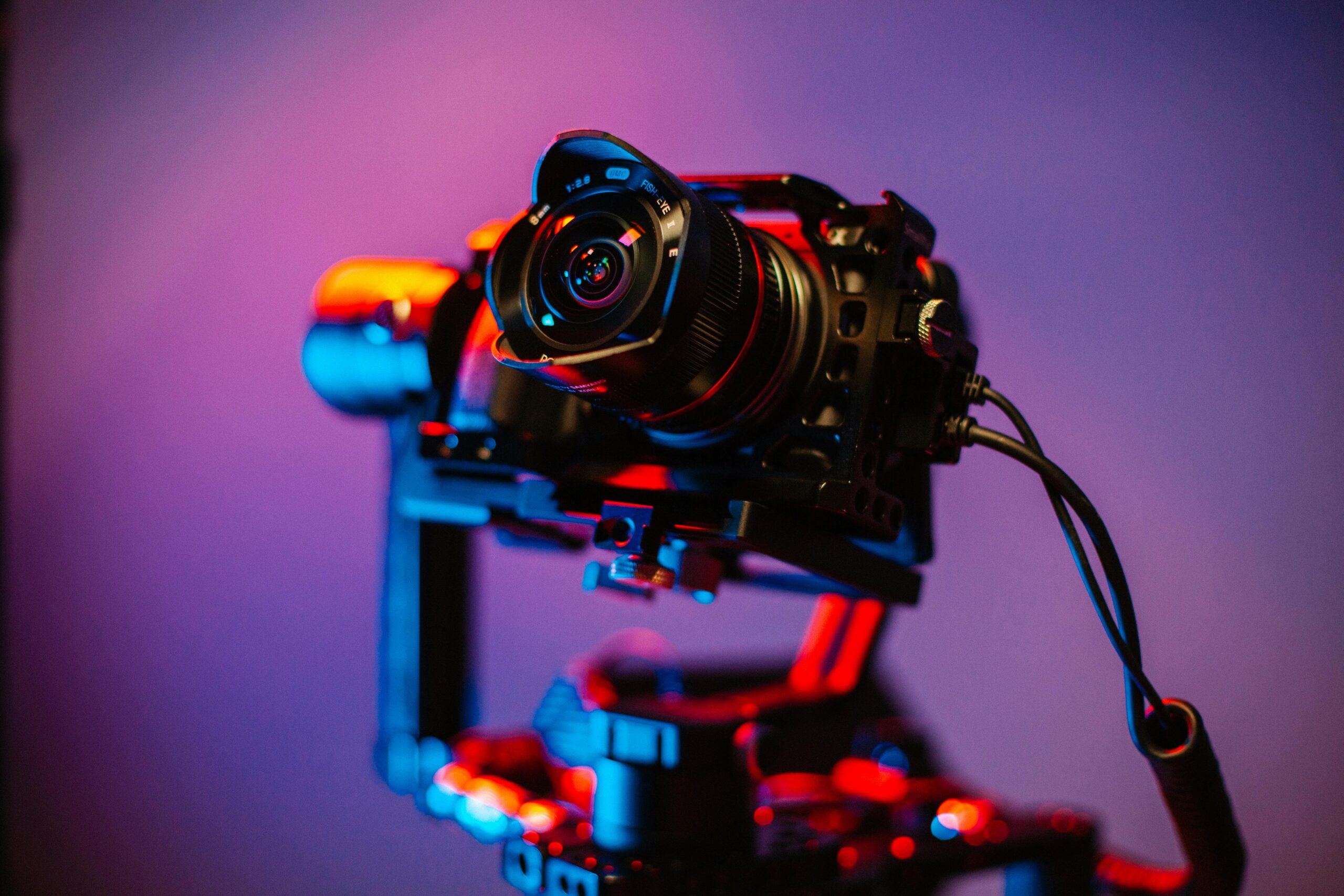 Close-up of a DSLR camera mounted on a gimbal with vibrant blue and red studio lighting.