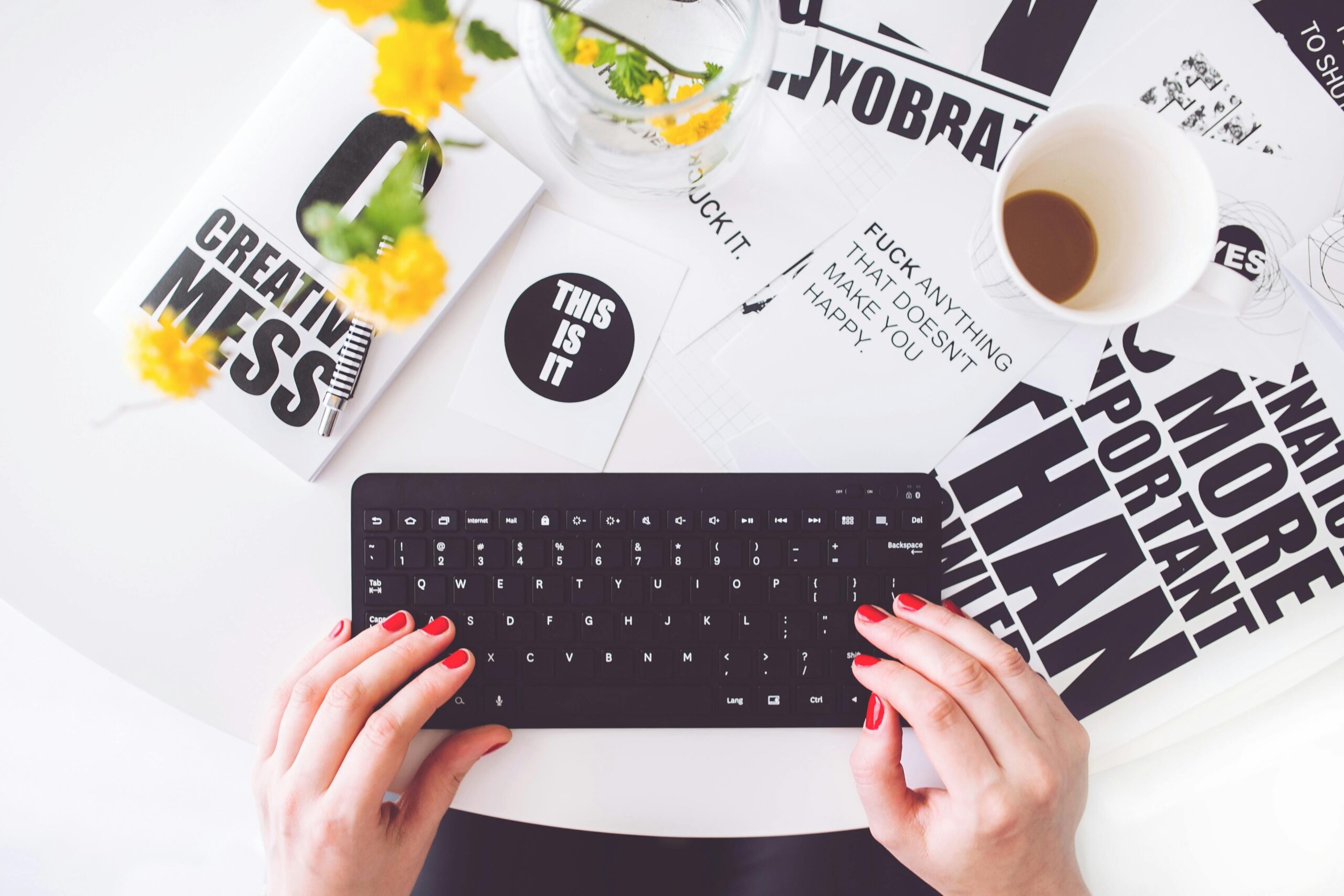 A creative workspace featuring a woman typing with red nails, surrounded by inspirational typography.