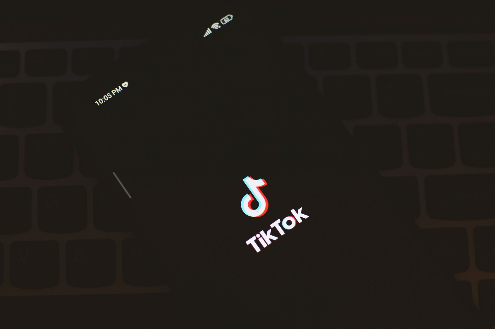 Close-up of a smartphone displaying the TikTok app logo against a dark keyboard background.