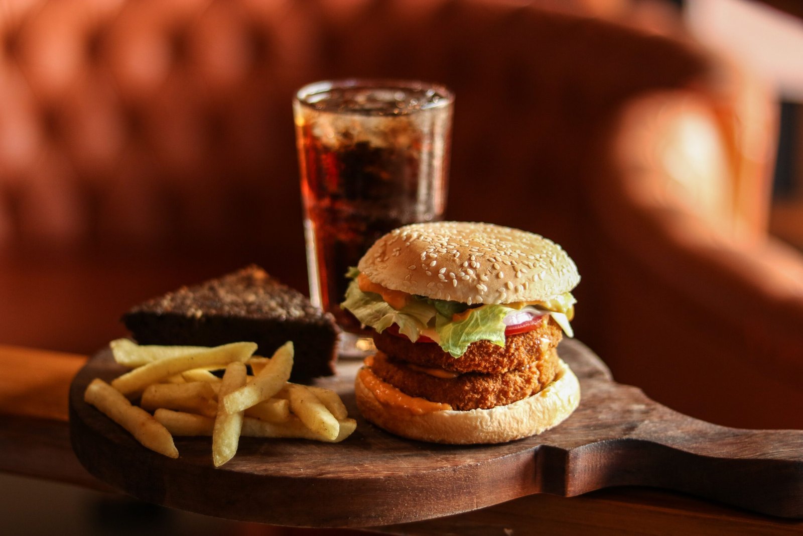 Tasty burger, fries, brownie, and cola on a wooden board for a satisfying meal.