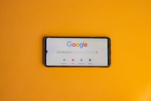 Smartphone displaying Google search page on a vibrant yellow background.