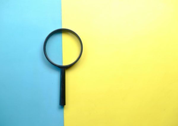 A magnifying glass lays on a split blue and yellow background in a flat lay style.