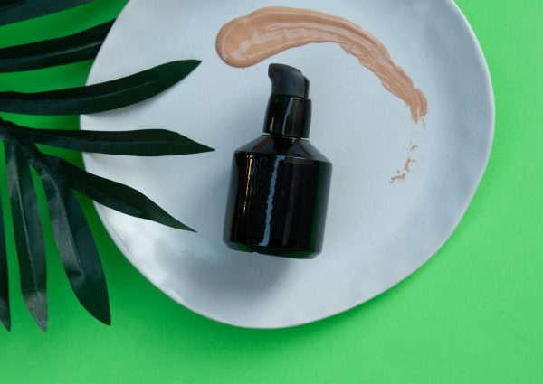 Black skincare pump bottle on a white plate with green leaf and makeup smear.